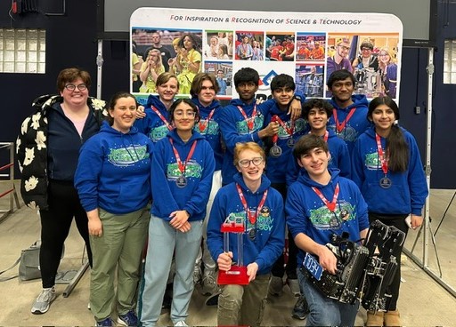A group of students wearing matching blue hoodies pose together indoors with a trophy.